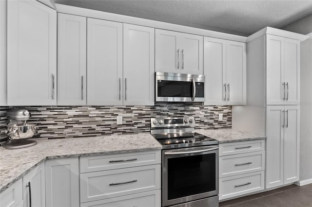 kitchen with tasteful backsplash, white cabinets, appliances with stainless steel finishes, light stone countertops, and a textured ceiling