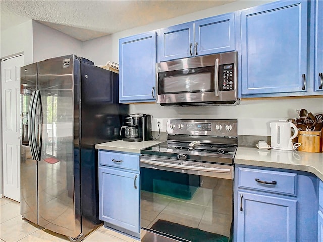 kitchen with appliances with stainless steel finishes, light countertops, blue cabinetry, and light tile patterned flooring