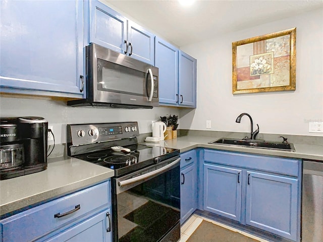 kitchen with blue cabinets, dark countertops, appliances with stainless steel finishes, and a sink