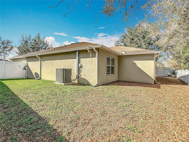 back of property featuring a lawn, stucco siding, fence, and central air condition unit