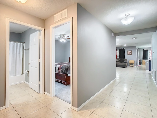 hall featuring visible vents, a textured ceiling, baseboards, and light tile patterned floors