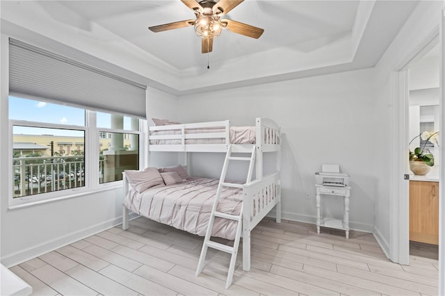 bedroom featuring ceiling fan, baseboards, a tray ceiling, and wood finish floors