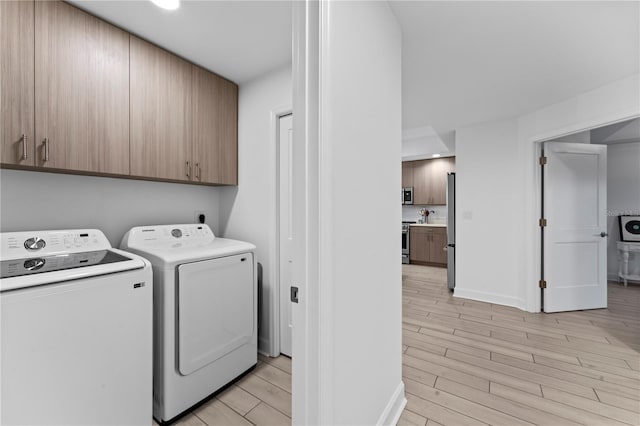 washroom featuring separate washer and dryer, light wood-style flooring, cabinet space, and baseboards