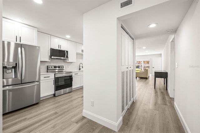 2101 Cordova Grn, Seminole, FL 33777 - kitchen with stainless steel appliances, light countertops, white cabinetry, and light wood-style floors