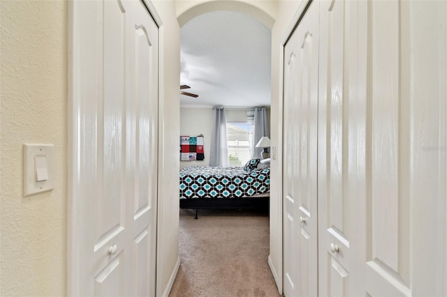 hall with arched walkways, a textured wall, and light colored carpet