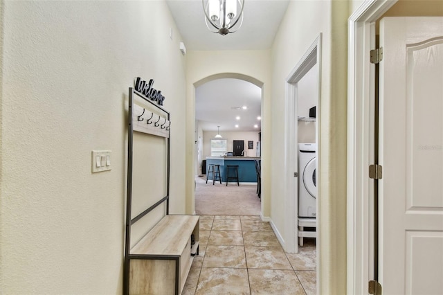 corridor featuring washer / dryer, arched walkways, baseboards, and light tile patterned floors