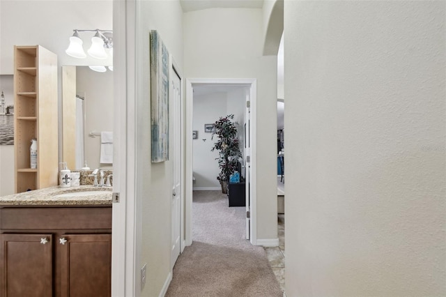 hallway with light carpet, a sink, and baseboards