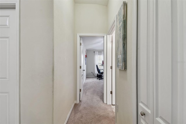 hallway featuring light colored carpet and baseboards