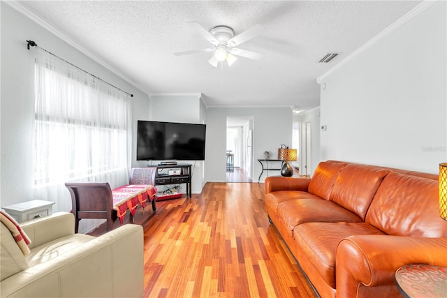 living area with a textured ceiling, ornamental molding, visible vents, and light wood-style floors