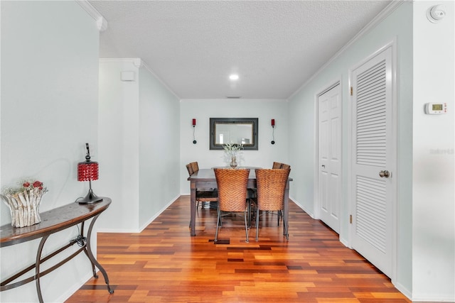 dining room with crown molding, a textured ceiling, baseboards, and wood finished floors