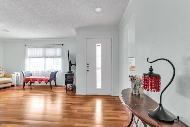 foyer entrance featuring baseboards, a textured ceiling, ornamental molding, and wood finished floors