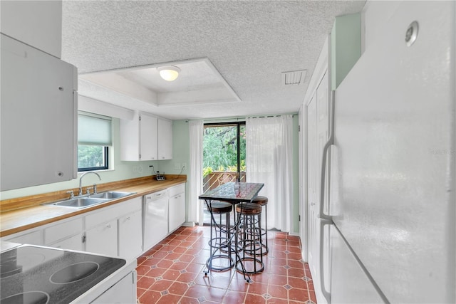 kitchen featuring a raised ceiling, white appliances, a sink, and white cabinets