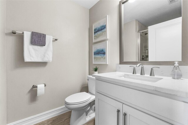 bathroom featuring a shower with shower door, toilet, wood finished floors, vanity, and baseboards