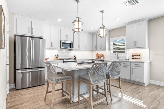 kitchen with visible vents, appliances with stainless steel finishes, a kitchen breakfast bar, light countertops, and light wood-style floors