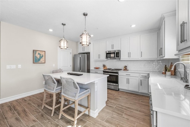 kitchen featuring appliances with stainless steel finishes, wood tiled floor, a sink, and decorative backsplash