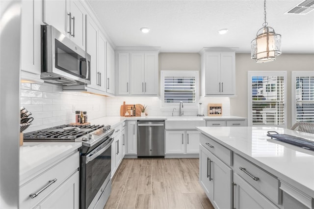 kitchen featuring decorative light fixtures, light wood finished floors, visible vents, appliances with stainless steel finishes, and a sink