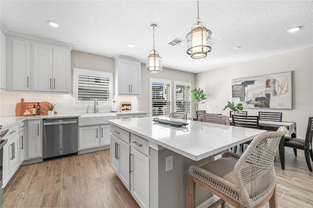 kitchen featuring wood finish floors, light countertops, visible vents, dishwasher, and a kitchen bar