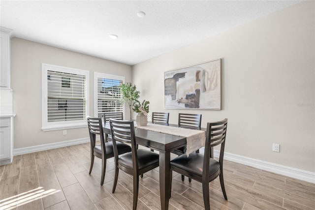 dining room with light wood-type flooring, a textured ceiling, and baseboards