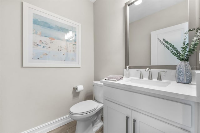 half bathroom featuring vanity, wood finished floors, toilet, and baseboards