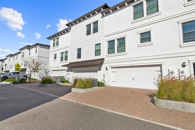 view of front facade with decorative driveway, stucco siding, an attached garage, central AC, and a residential view