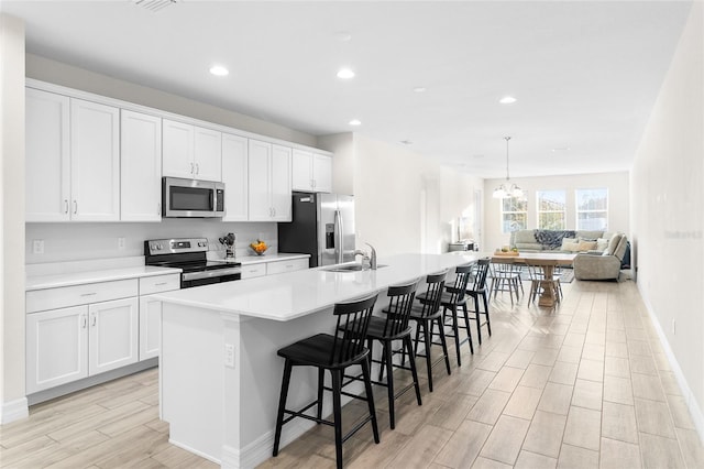 kitchen with light countertops, appliances with stainless steel finishes, a kitchen island with sink, and white cabinets