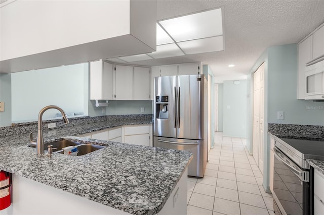 kitchen featuring dark stone counters, a peninsula, stainless steel appliances, white cabinetry, and a sink