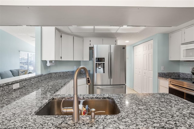 kitchen with stainless steel appliances, dark stone countertops, a sink, and white cabinetry