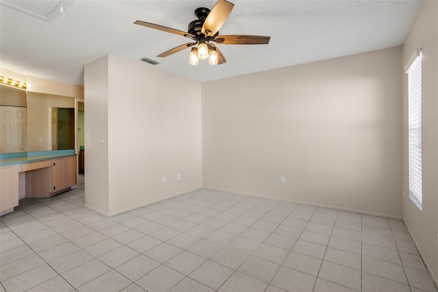 spare room featuring light tile patterned flooring, plenty of natural light, a textured ceiling, and ceiling fan