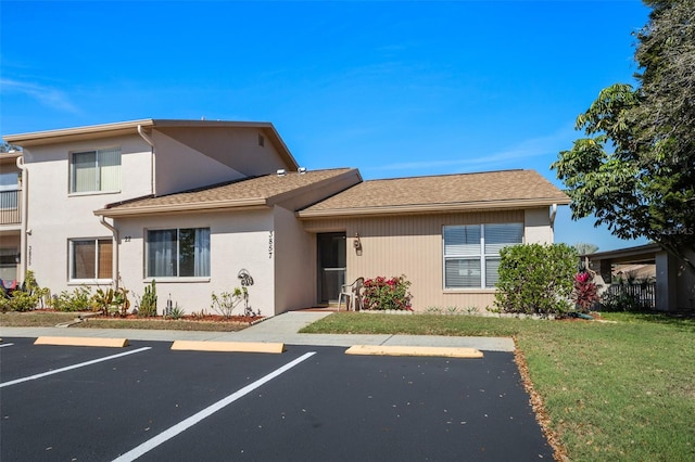 view of front of home with stucco siding, a shingled roof, uncovered parking, and a front yard