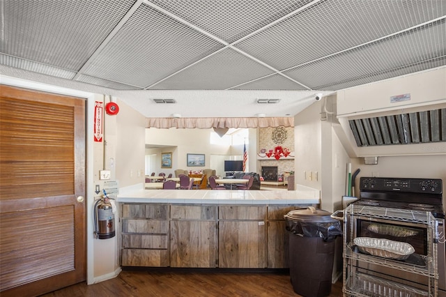 kitchen with tile countertops, visible vents, electric range oven, dark wood-type flooring, and a large fireplace