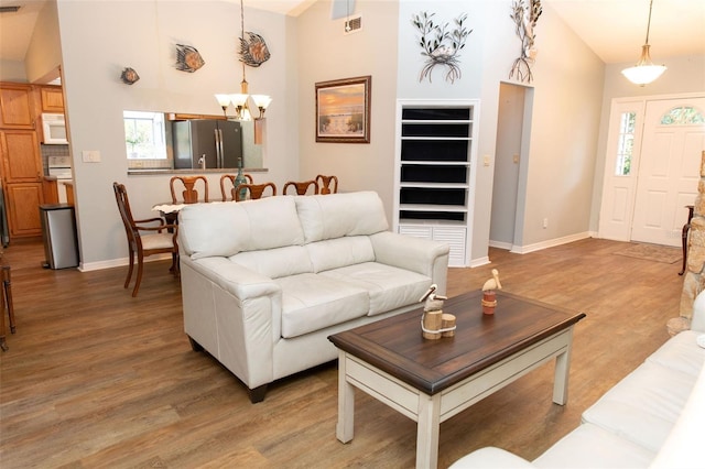 living area with light wood-style floors, baseboards, high vaulted ceiling, and an inviting chandelier