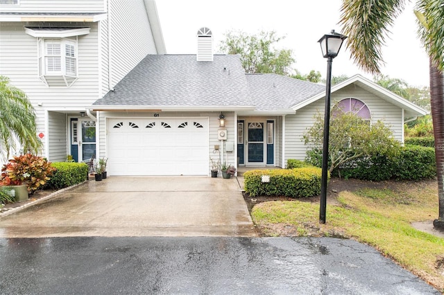 view of front of house with a garage, driveway, a chimney, and a shingled roof