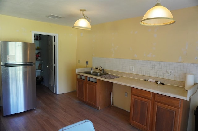 kitchen featuring visible vents, brown cabinetry, dark wood-style flooring, freestanding refrigerator, and a sink