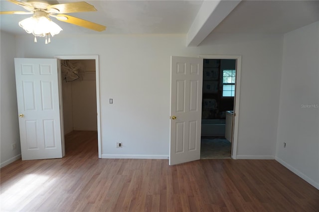 unfurnished bedroom featuring a closet, a spacious closet, ensuite bathroom, wood finished floors, and baseboards