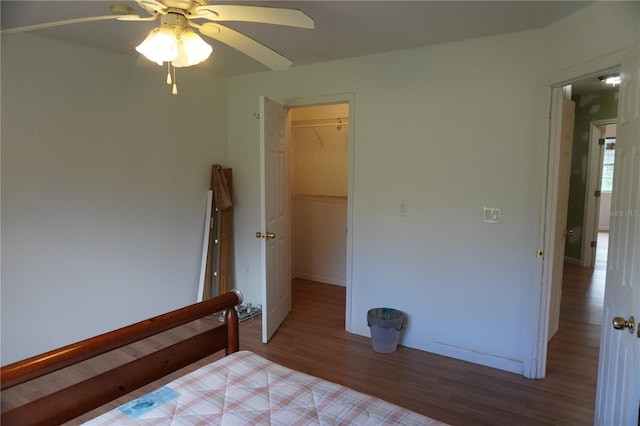 unfurnished bedroom featuring a closet, a spacious closet, a ceiling fan, wood finished floors, and baseboards