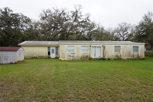 rear view of property with metal roof, a lawn, and stucco siding