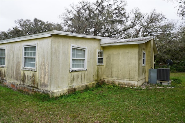 view of side of home featuring metal roof, central AC unit, and a lawn