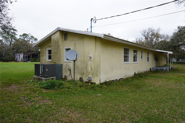 view of side of property with a yard, central AC, and stucco siding