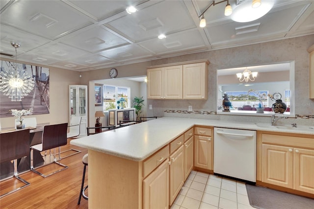 kitchen with light countertops, white dishwasher, a peninsula, and a notable chandelier