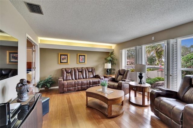 living room featuring light wood-type flooring, visible vents, and a wealth of natural light