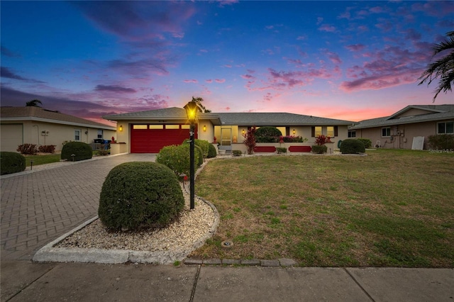 ranch-style house featuring a front lawn, decorative driveway, an attached garage, and stucco siding