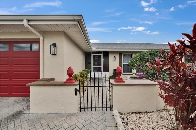 property entrance featuring a garage, roof with shingles, a gate, and stucco siding