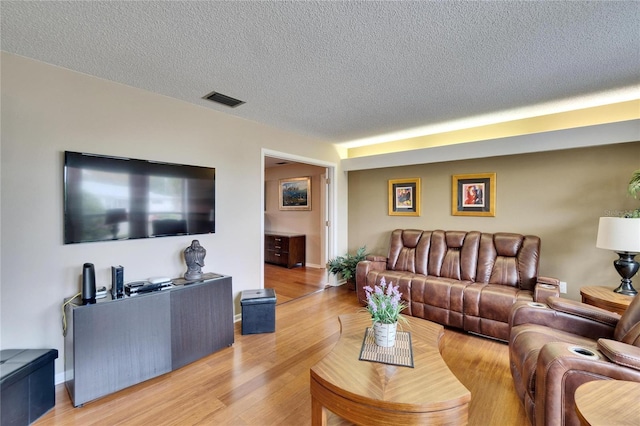 living area with light wood-type flooring, visible vents, a textured ceiling, and baseboards