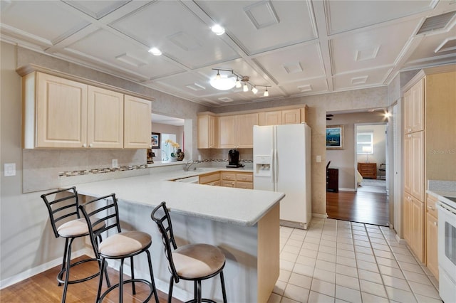 kitchen featuring white appliances, coffered ceiling, a peninsula, light countertops, and a kitchen bar