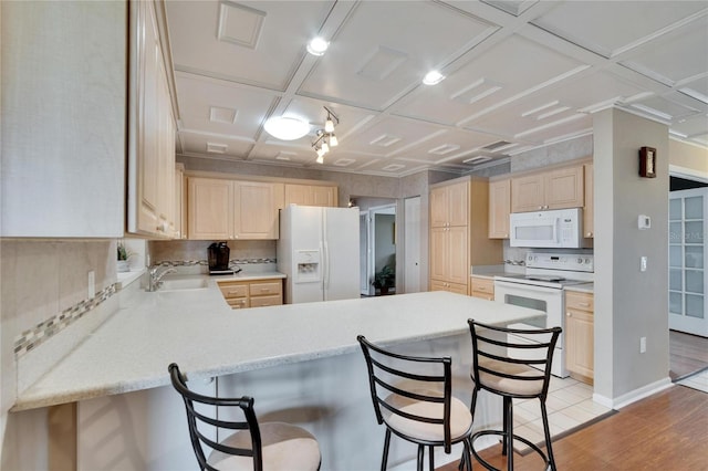 kitchen featuring white appliances, a breakfast bar area, a peninsula, light countertops, and a sink