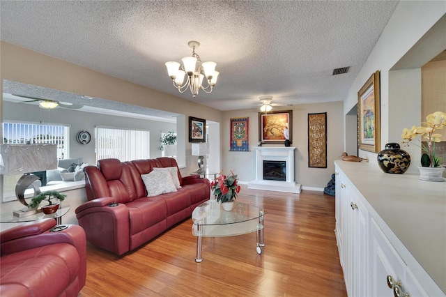 living room with a glass covered fireplace, light wood-style flooring, a textured ceiling, and ceiling fan with notable chandelier