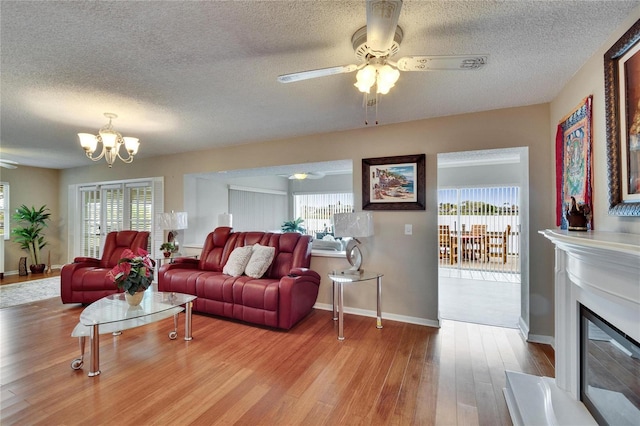 living room featuring ceiling fan with notable chandelier, a wealth of natural light, a glass covered fireplace, and wood finished floors