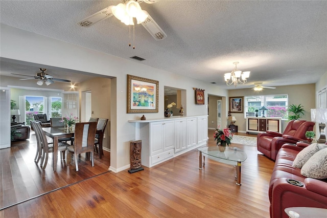 living area with ceiling fan with notable chandelier, light wood finished floors, visible vents, and a wealth of natural light