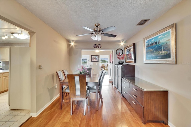 dining area featuring light wood finished floors, visible vents, baseboards, ceiling fan, and a textured ceiling