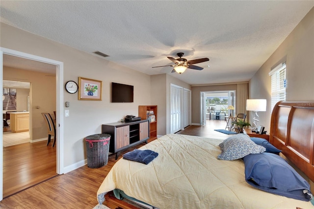 bedroom featuring visible vents, a ceiling fan, a textured ceiling, wood finished floors, and baseboards